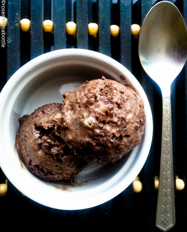 Two scoops of chocolate ice cream in a white circular bowl,
    with a silver tablespoon lying alongside it, viewed from overhead