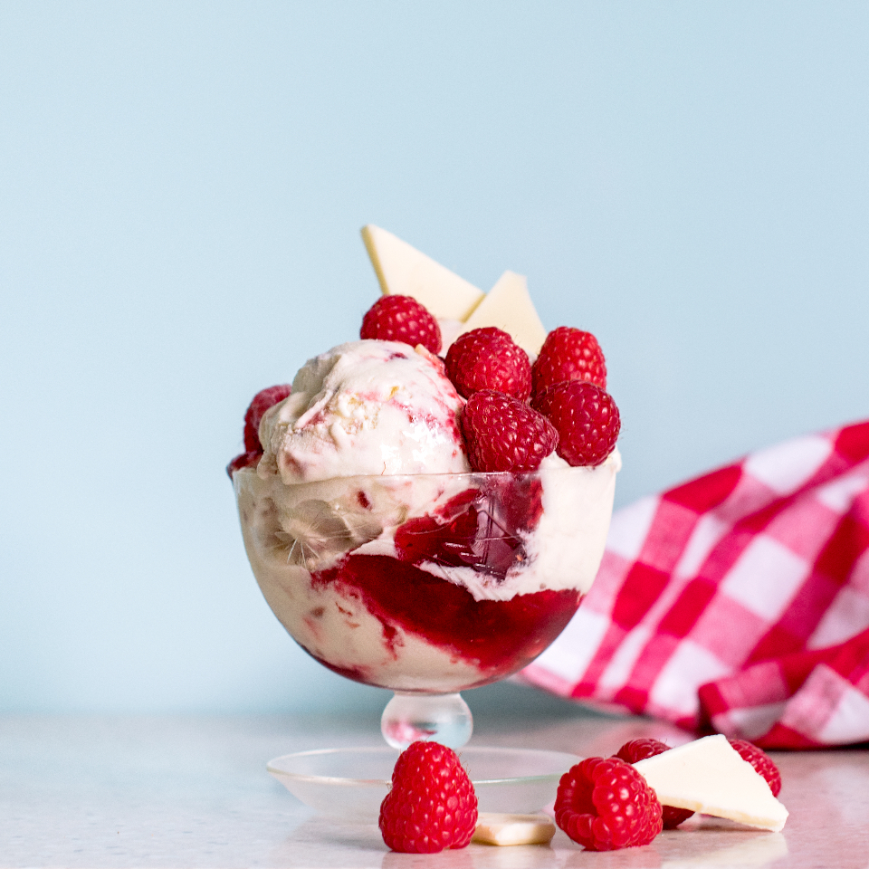 Red and white strawberry ripple ice cream filling a round transparent glass bowl, 
    with several strawberries placed on top and four more lying around its circular glass 
    base, against a very pale blue background